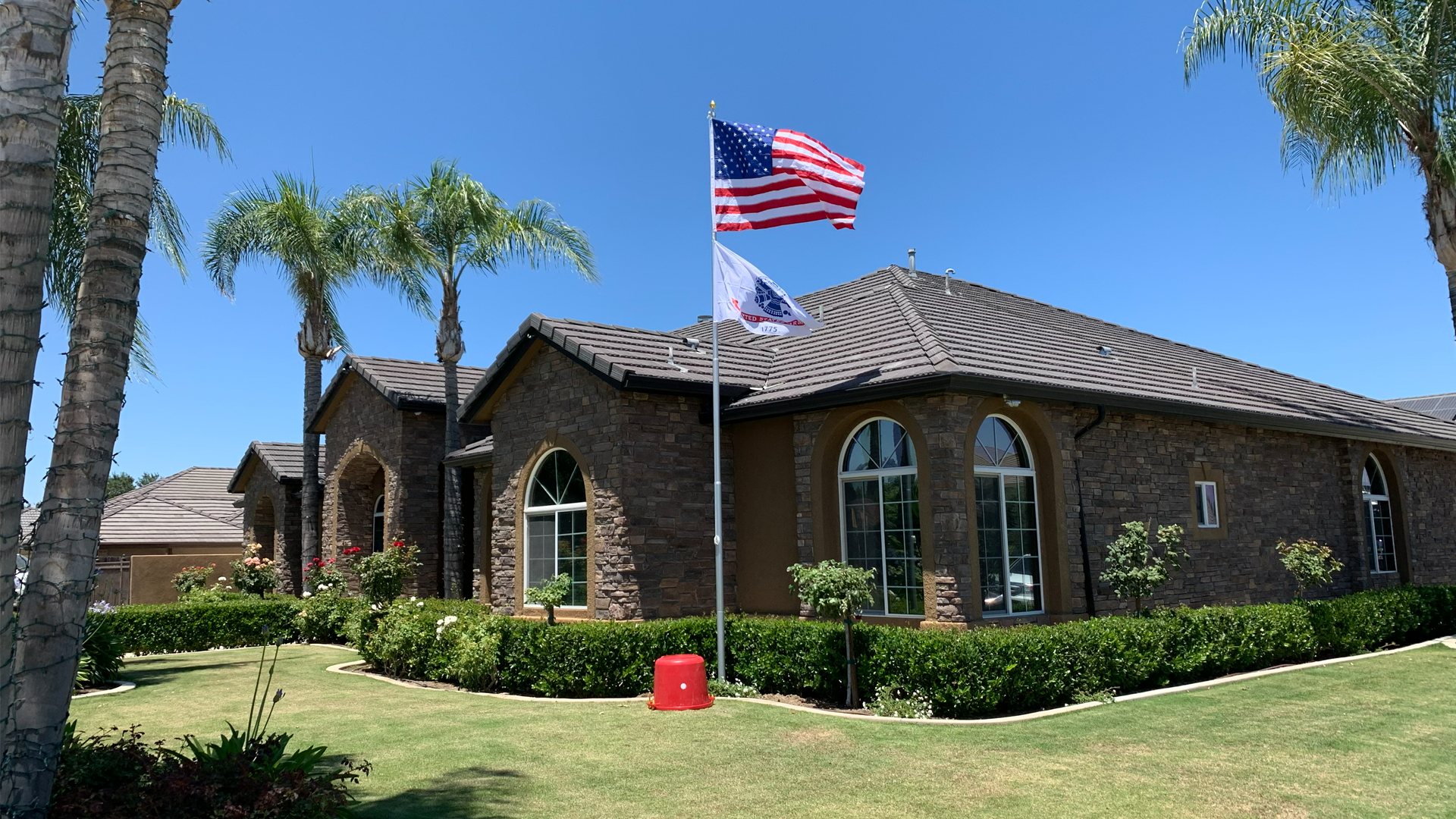 American flag waving on a flagpole in front of a residential house with a clear blue sky background.